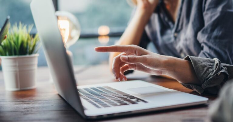 A person's hand pointing to a laptop computer with another person next to them