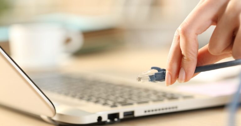 Fingers holding ethernet cable about to plug into laptop